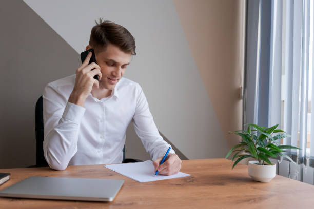 istock A man is talking on his cell phone while writing on a piece of paper 2157107094