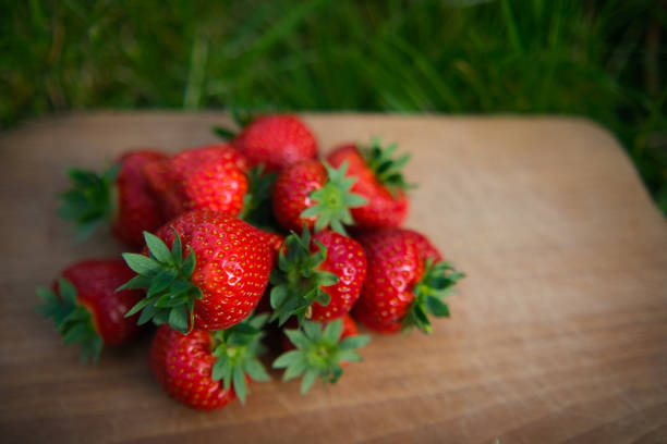 Small stack of large strawberries on a wooden board on the grass. High angle view.