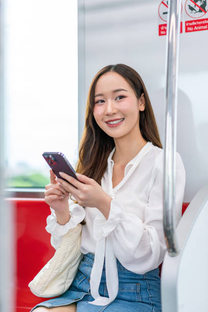istock Asian woman sitting on a metro skytrain, using her phone and looking away 2157112965