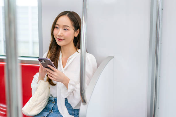istock Asian woman sitting on a metro skytrain, using her phone and looking away 2157112972