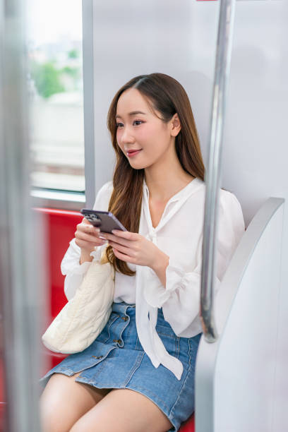 istock Asian woman sitting on a metro skytrain, using her phone and looking away 2157113011