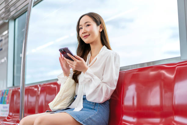 istock Asian woman sitting on a metro skytrain, using her phone and looking away 2157113055