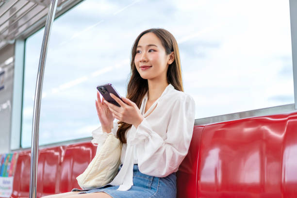 istock Asian woman sitting on a metro skytrain, using her phone and looking away 2157113089