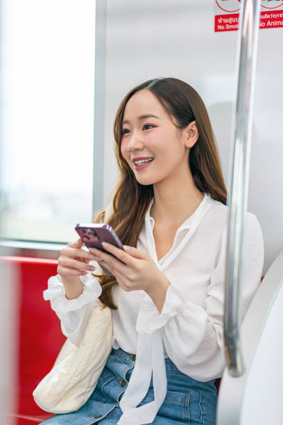 istock Asian woman sitting on a metro skytrain, using her phone and looking away 2157113103