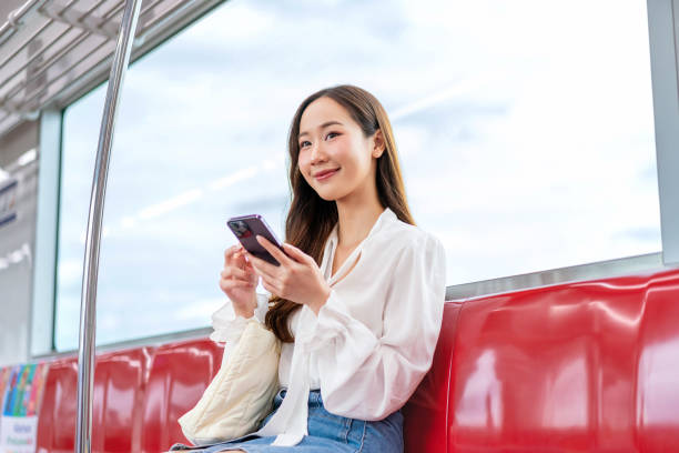 Asian woman sitting on a metro skytrain, using her phone and looking away