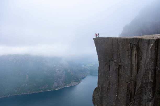 istock A panoramic view from the edge of Preikestolen, a cliff in Norway, showcasing two figures standing on the edge, overlooking a misty fjord 2157113129