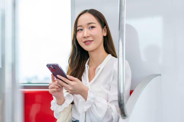 istock Asian woman sitting on a metro skytrain, using her phone and looking away 2157113147