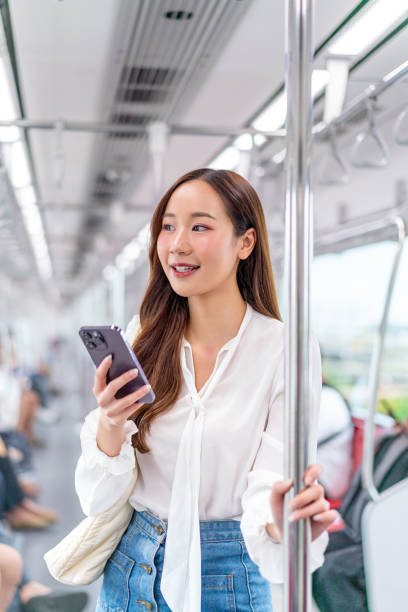 istock Asian woman standing on a metro skytrain, using her phone and looking away 2157113265