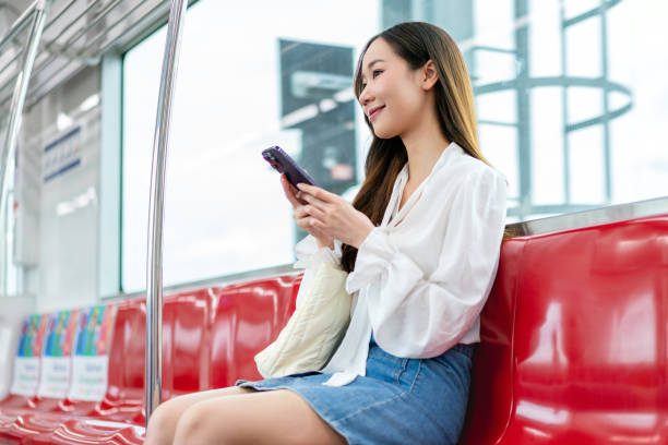 istock Asian woman sitting on a metro skytrain, using her phone and looking away 2157113321