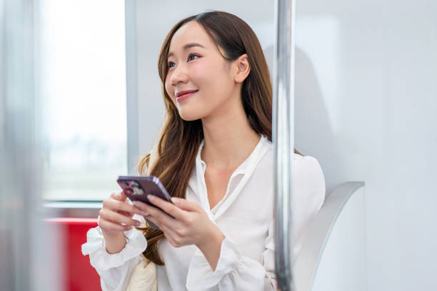 istock Asian woman sitting on a metro skytrain, using her phone and looking away 2157113327