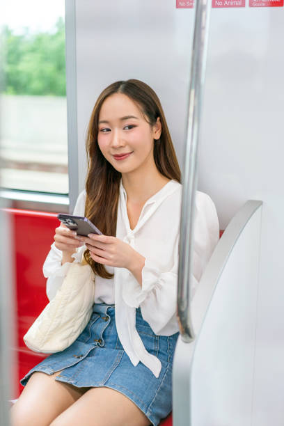 istock Asian woman sitting on a metro skytrain, using her phone and looking away 2157113545