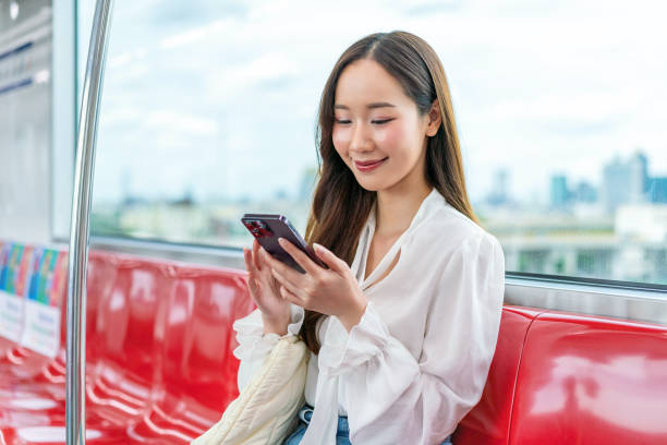 istock Asian woman sitting and using phone while commuting on a metro skytrain. Background is beautiful cityscape 2157113724
