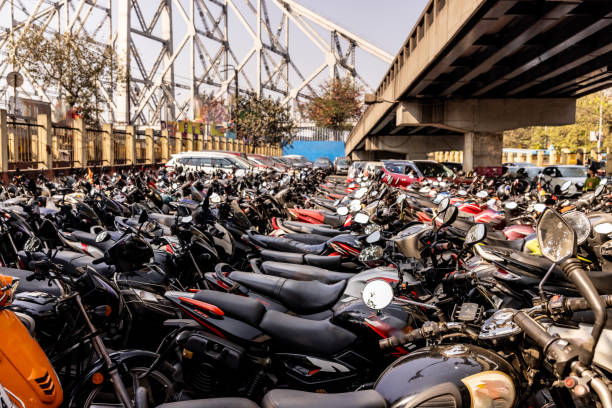 Various motor vehicles parked in line under overpass with Howrah bridge in background in Kolkata city during sunny day