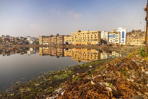 View of garbage dump on riverbank with residential district in background against clear blue sky