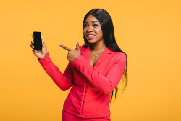 istock A cheerful African woman presenting smartphone on a yellow background 2157124410