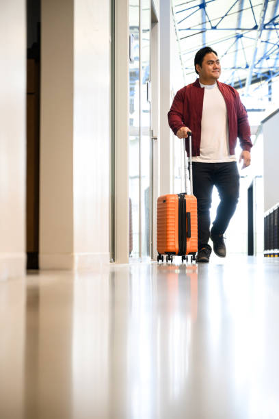 istock Full length man walking in office building  with small wheeled luggage 2157129347