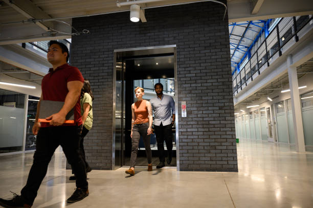 istock Co-workers walk out of lift in building atrium 2157129528