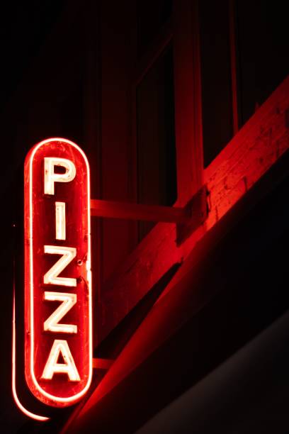 istock Neon sign for a pizza restaurant glowing brightly against a dark background. 2157130043