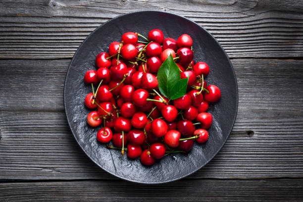 Black plate with ripe cherries on top on a rustic wooden table