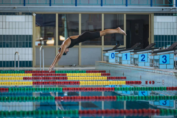 Professional female swimmer preparing and jumping off the starting block into the pool. Competitive swimmers workout concept.