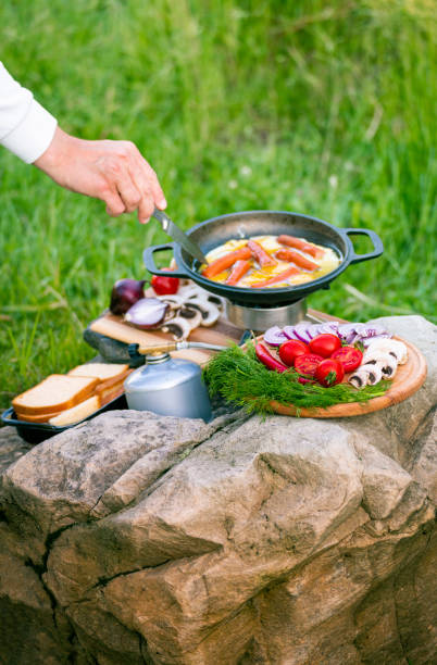 A person uses a slotted utensil to cook french fries wedges over an open flame in a rustic outdoor environment, showcasing traditional outdoor cooking techniques and a focus on simplicity