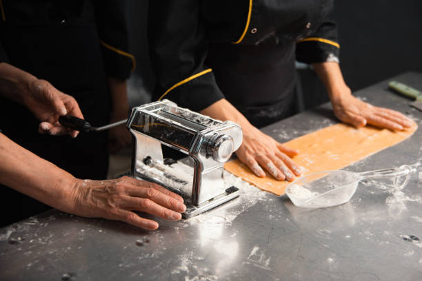 Professional chefs are utilizing a traditional pasta machine for crafting fresh pasta dough stock photo