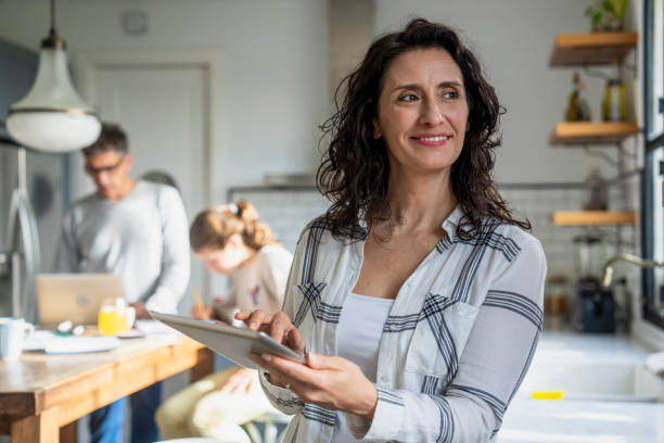 istock Woman checking messages on digital tablet while husband is helping daughter with homework in background 2157154717