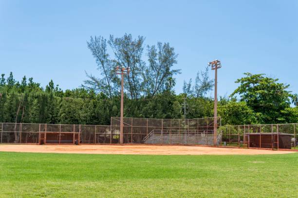 istock Empty baseball field with green grass, benches, and trees in the background under a clear blue sky 2157160499