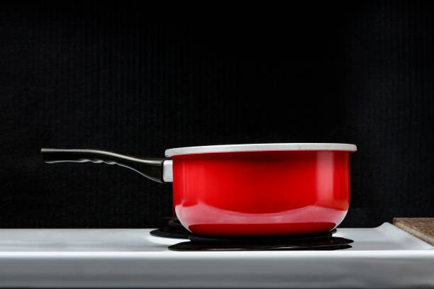 Horizontal shot of a red pot on a stove top electric burner with a black background.  Side view.  Copy space.