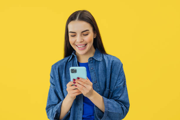 istock Smiling young brunette woman girl in yellow studio using mobile phone, typing sms message 2157161618
