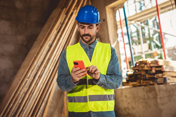 istock Construction site manager standing  wearing safety vest and helmet, using his phone at construction site. 2157172187