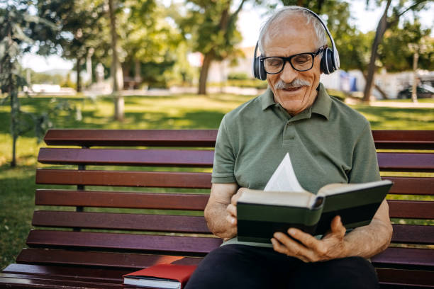 istock Senior man enjoying in hobbies reading a book while sitting in public park on bench 2157176357