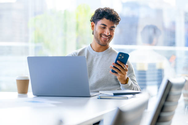 Businessman working on a laptop computer and texting or using social media on a mobile phone in the office