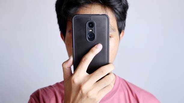 close-up of a man's face covered by his smartphone close-up of a man's face covered by his smartphone with a white background person holding frame over face stock pictures, royalty-free photos & images