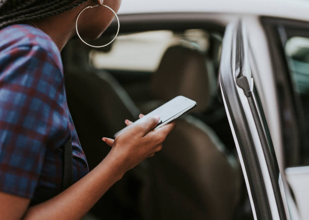 istock Black woman holding her phone while getting into a car 2157195844