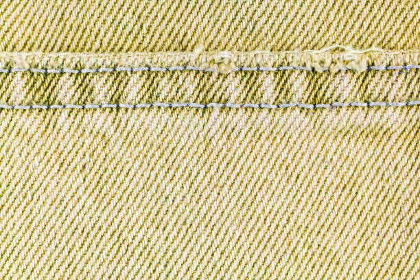 Yellow denim jeans pants cloth with seam, close up, macro. Fabric texture wallpaper, backdrop, design detail.