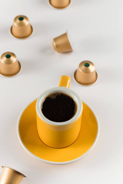 Yellow coffee cup with golden coffee capsules on a white background, emphasizing a modern and convenient coffee brewing experience.