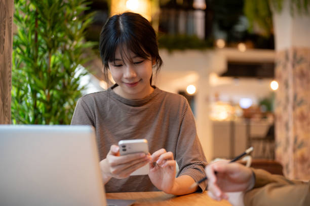 istock Beautiful Asian woman is reading messages on her smartphone while working remotely in a coffee shop. 2157219913