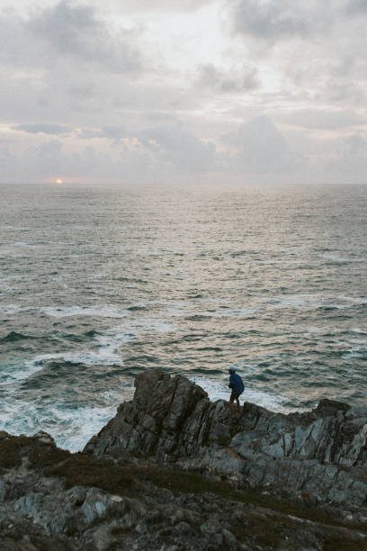 istock Man standing on the rocks by the beach at sunset 2157232792