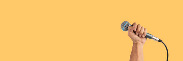 istock Black male hand holding a microphone isolated on yellow banner background 2157238615