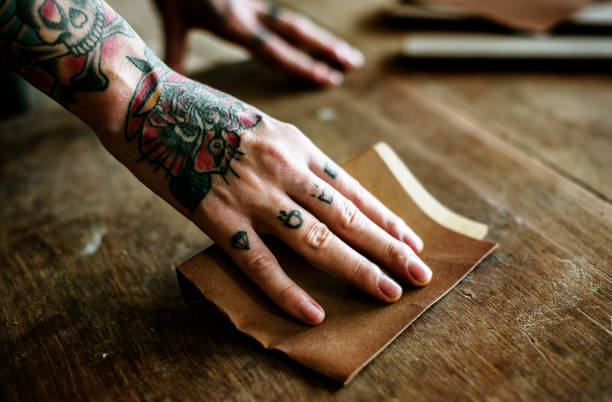 istock Hands with tattoo using sandpaper on a wood 2157245824