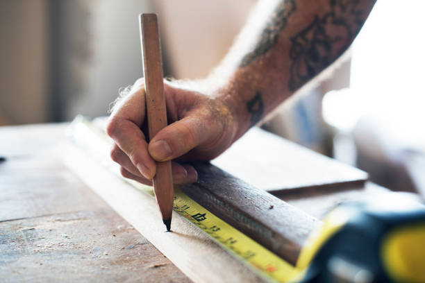 Carpenter using pencil and measurement tape on wood