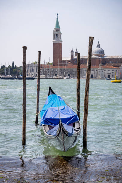 Venice, Italy - June 7th 2024:  Moored gondola under tarpaulins at the side of a canal in the center of Venice and with a view to a church tower