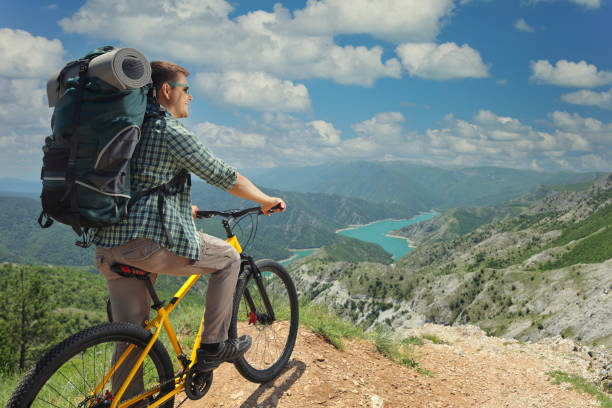 Man with a bicycle standing on the edge of a mountain cliff and looking at a lake