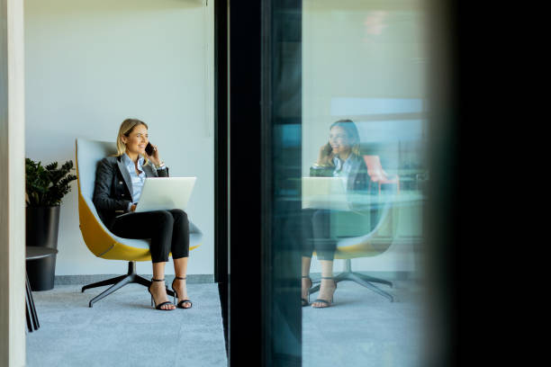 istock Businesswoman in modern office talking on phone and using laptop during daytime 2157252438