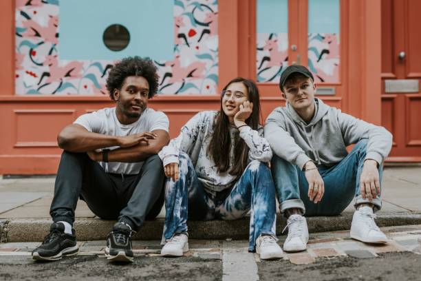 istock Diverse friends sitting on sidewalk in front of store 2157253623
