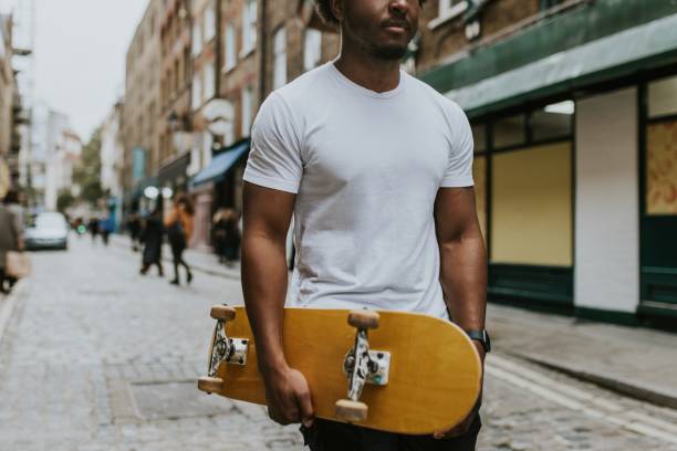 istock Man in white tee walking in town with wooden skateboard 2157253992