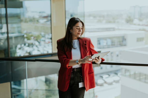 istock Smiling businesswoman in red blazer using tablet at modern office window in daylight 2157254232