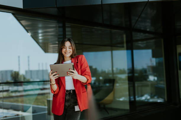 istock Smiling businesswoman in red blazer using tablet at modern office window in daylight 2157254233