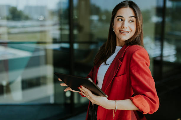 istock Smiling businesswoman in red blazer using tablet at modern office window in daylight 2157254238